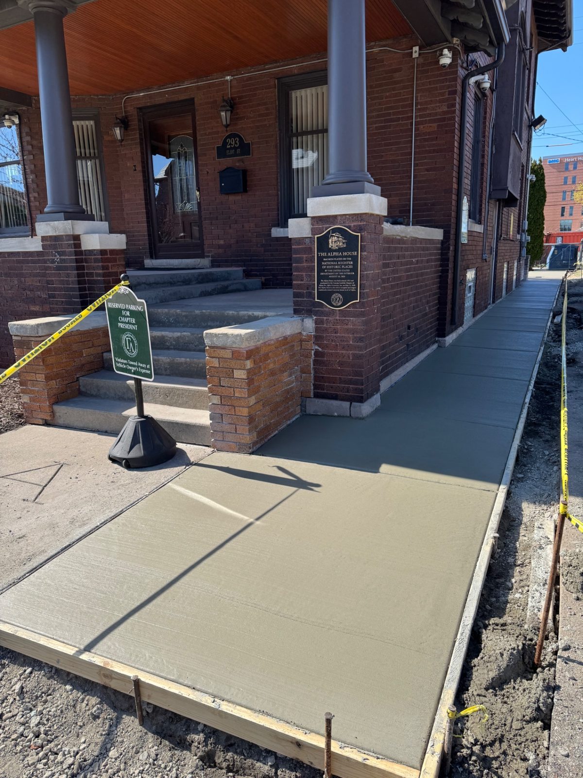 Freshly broomed concrete entry walkway held in wooden forms alongside a historic brick building with porch columns