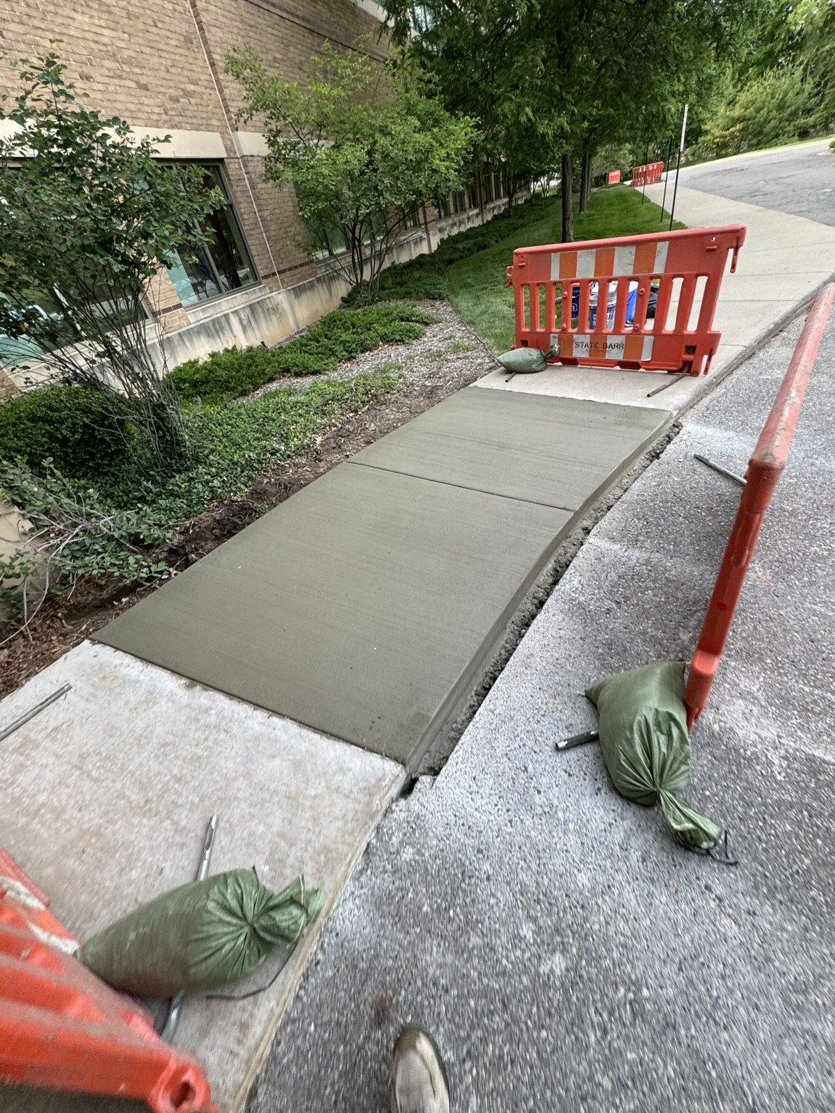 Commercial concrete sidewalk section replacement with orange safety barricades in place