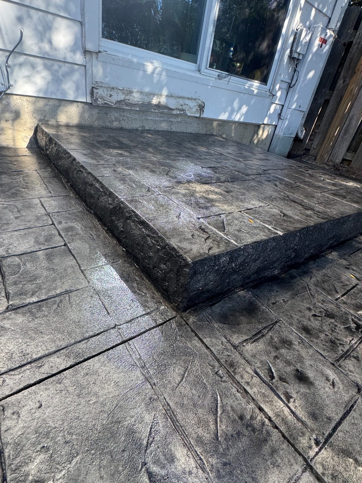 Close-up of a raised stamped concrete landing with textured rock-face edge on a slate-pattern stamped patio