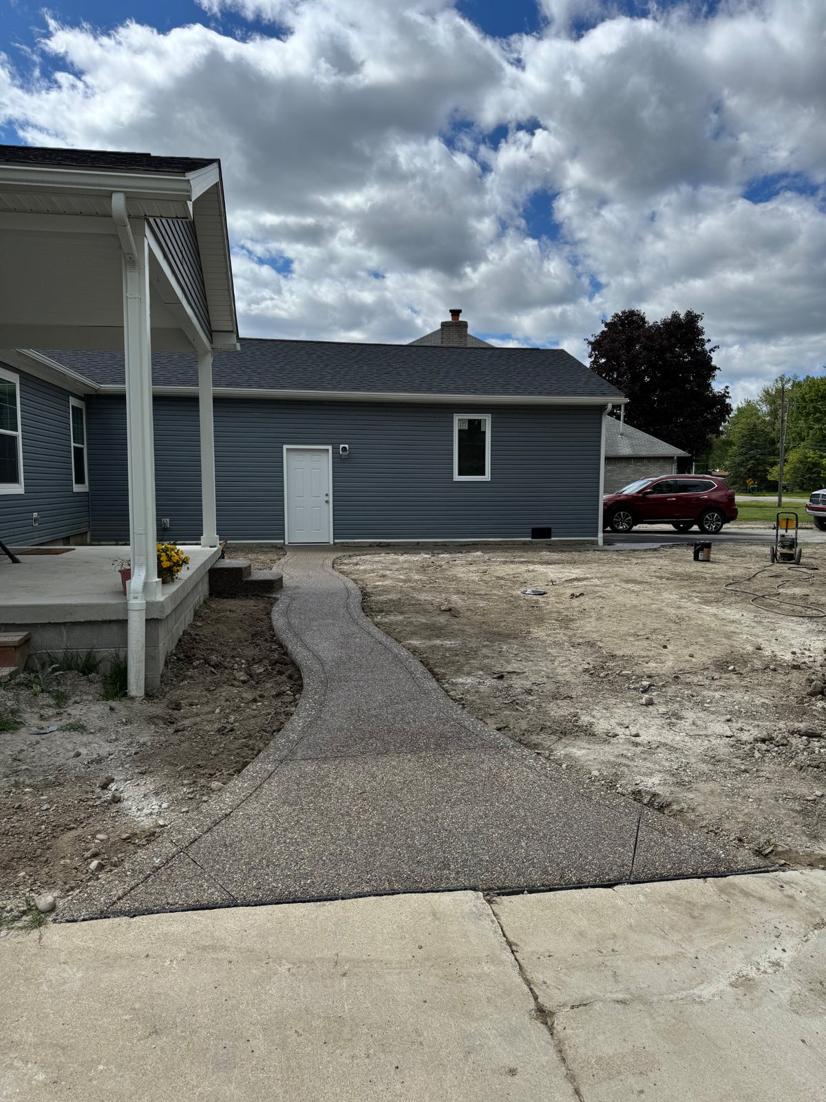 Curved exposed aggregate walkway connecting a driveway to a covered porch and side entry