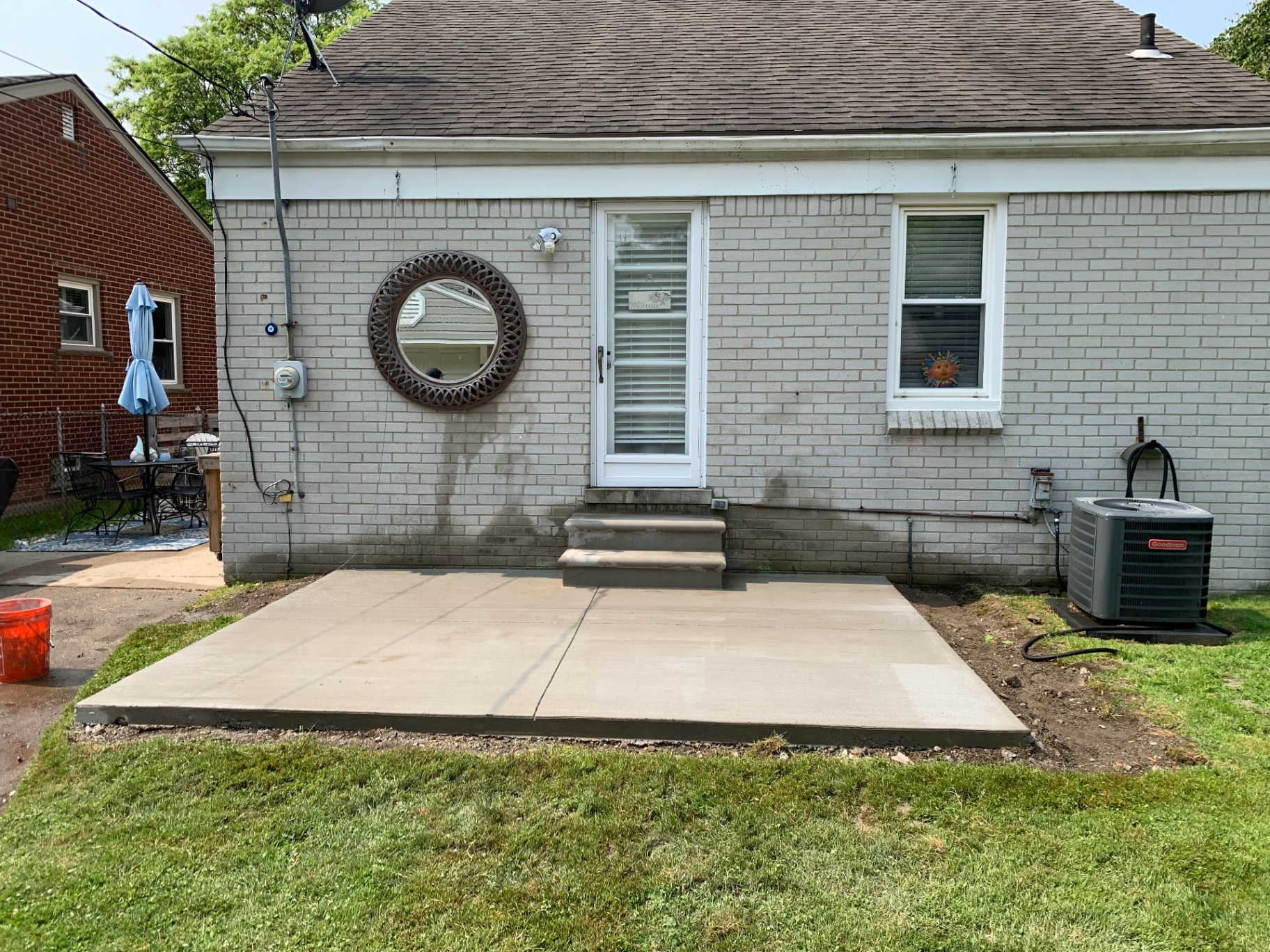 Broom-finish concrete patio with new steps at the back door of a white painted brick home