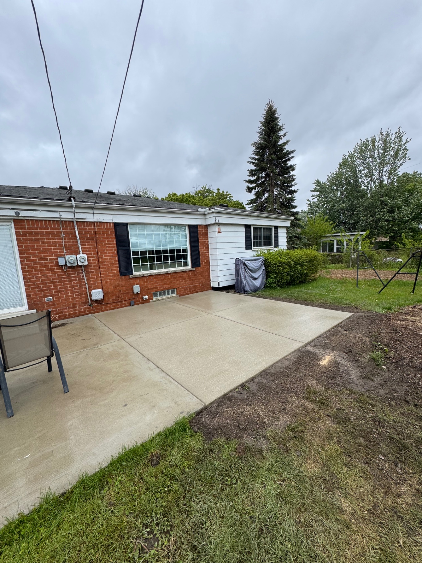 Fresh broom-finish concrete patio off the back of a red brick ranch home