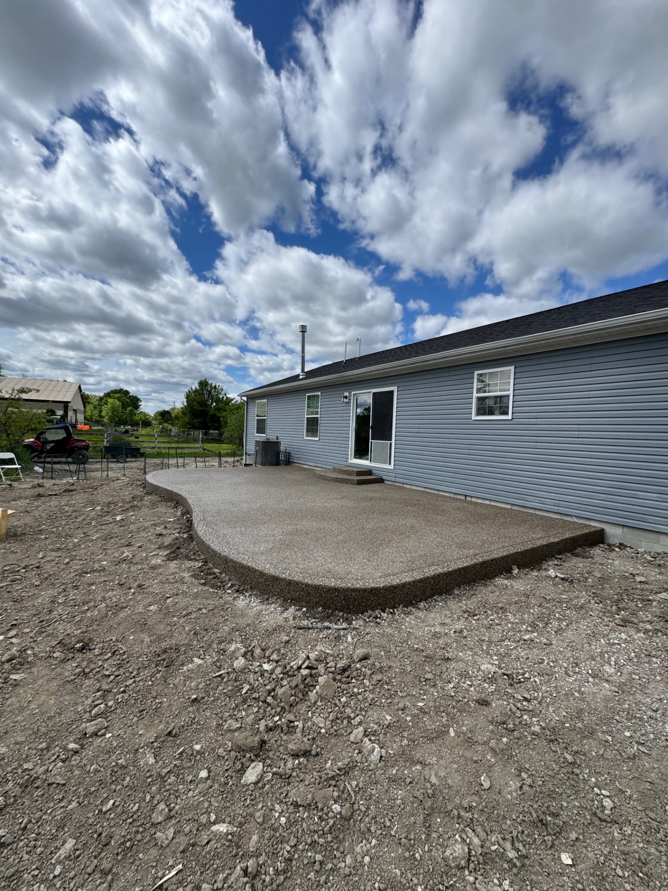 Curved exposed aggregate backyard patio and matching entry steps beside a gray-sided home