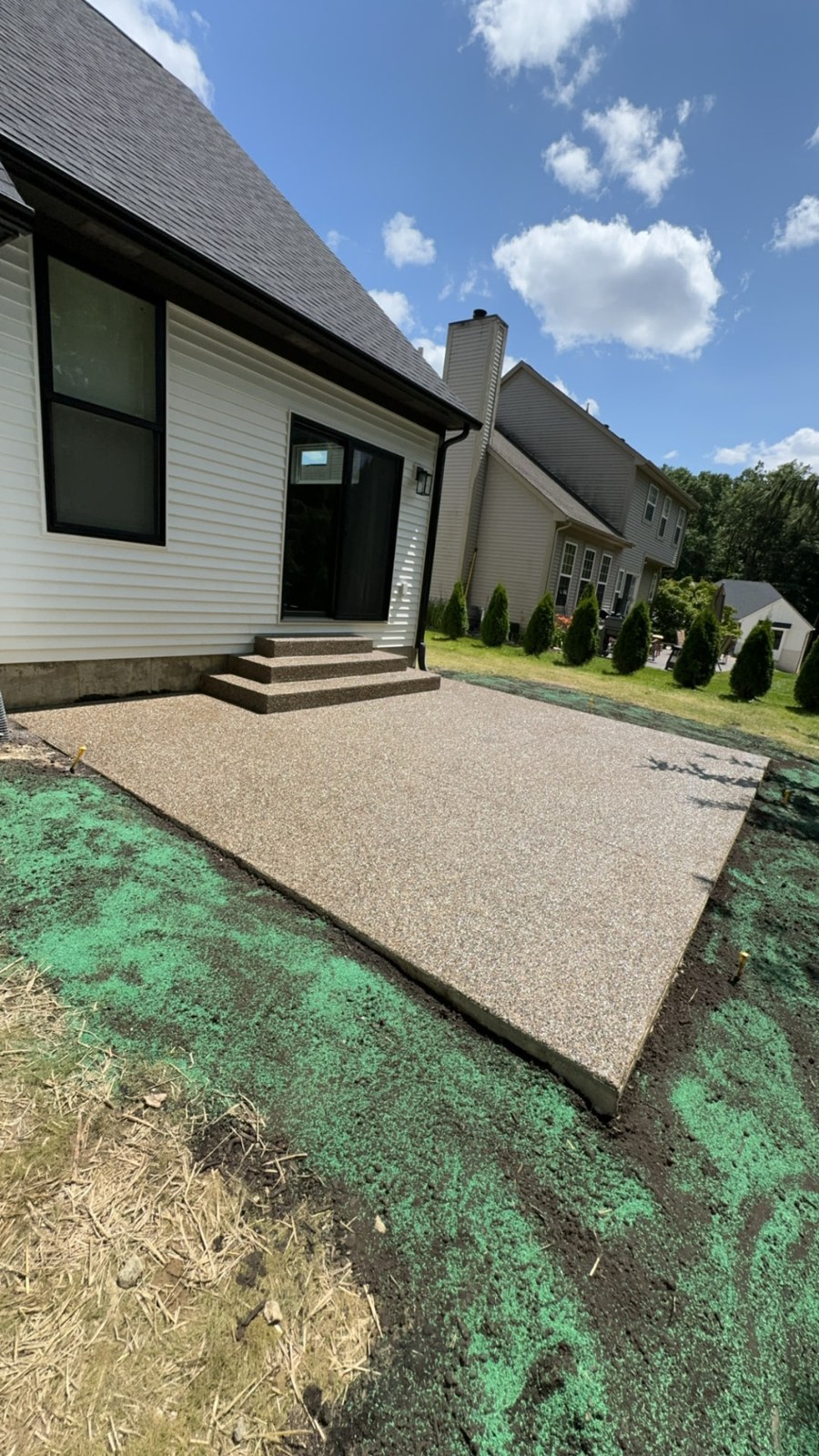 Exposed aggregate concrete patio and steps at the rear of a home with white siding