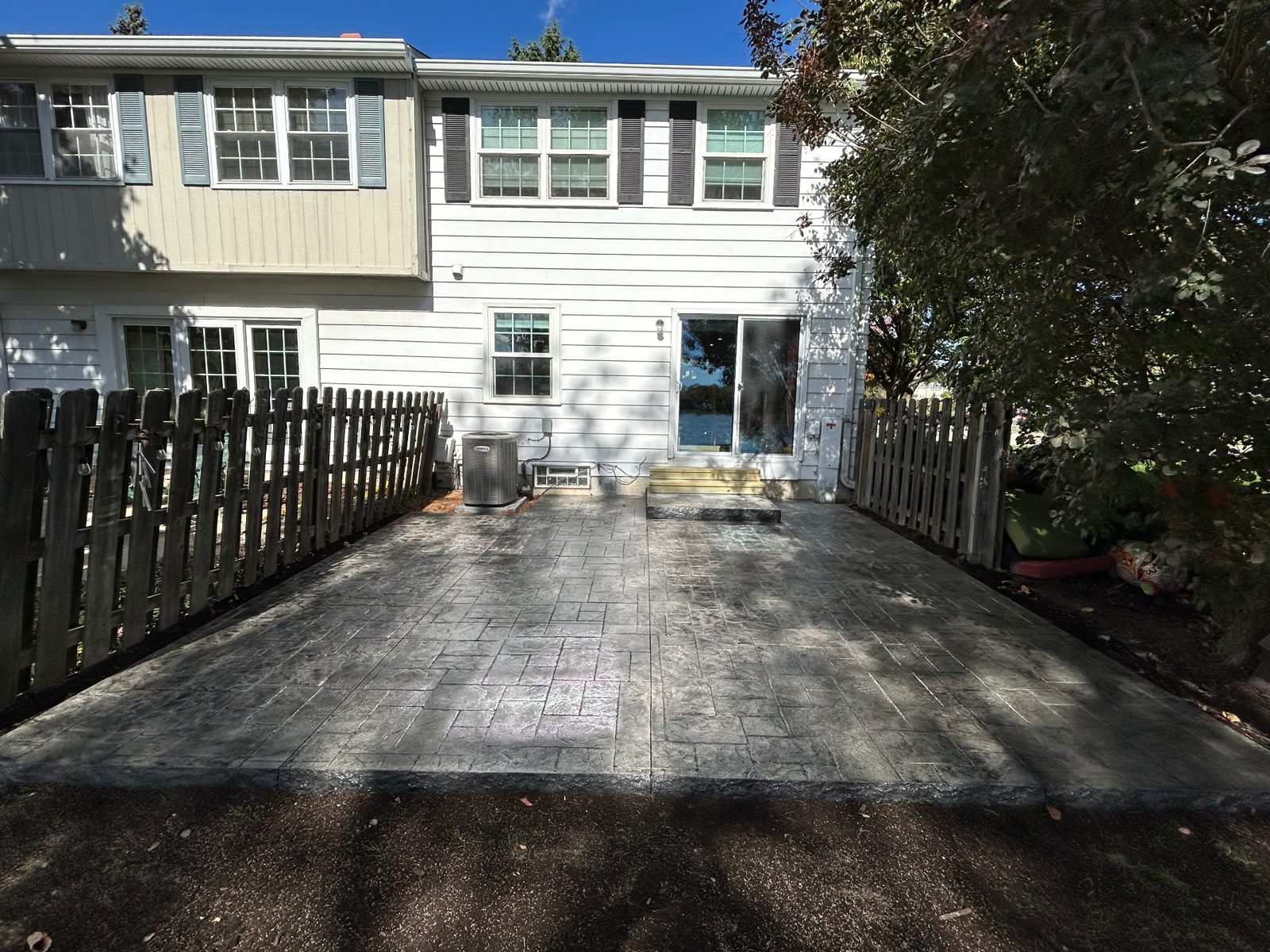 New gray stamped concrete patio with ashlar slate pattern and raised stamped step behind a two-story Southeast Michigan home