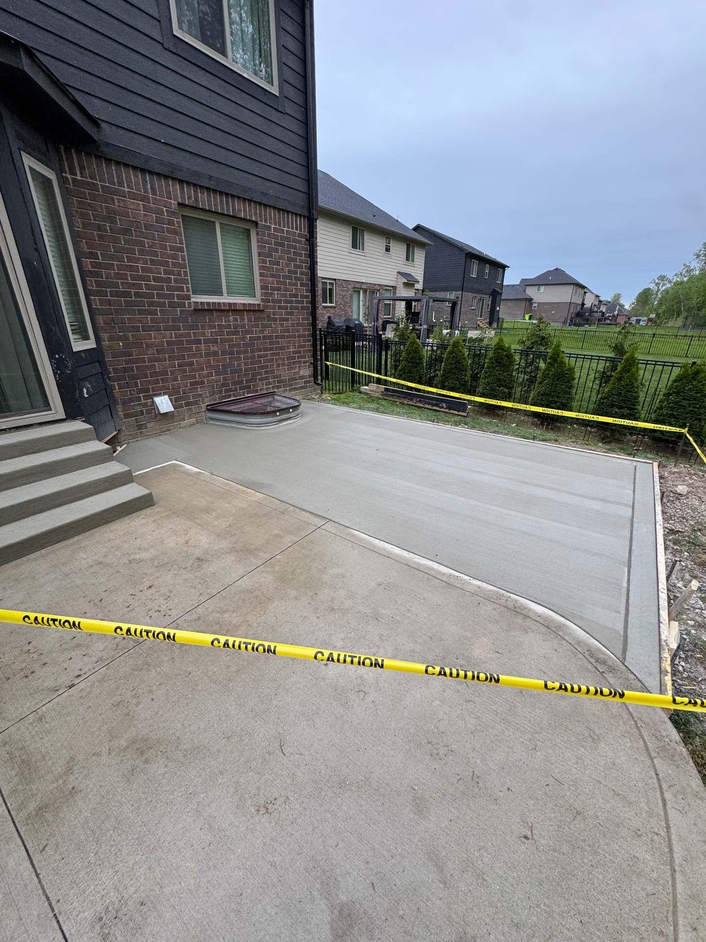 New broom-finish concrete patio with a curved edge behind a two-story home
